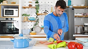 Young sporty man cutting and cooking fresh natural vegetables at kitchen and cooking for healthy lunch. Self care yoga nutritionis
