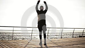 Young sporty man exercising on the dock near the seaside. Beautiful sunny morning on the seacoast. Outdoors footage.