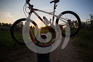 A young sporty man is holding a bicycle at sunset