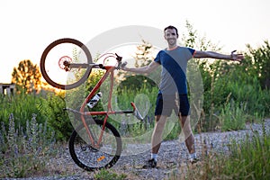 A young sporty man is holding a bicycle at sunset