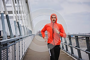Young sporty man in orange windbreaker jacket jogging on a cloudy day