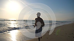Young sporty man running on the sea beach during sunrise. Athletic boy jogging along ocean coast. Male sportsman