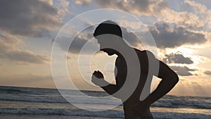 Young sporty man running on the sea beach at sunset. Athletic guy jogging along ocean shore during sunrise. Male