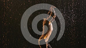 Young sporty man sexy dancing in the rain in an unbuttoned white shirt. Wet clothing hugs the muscular body. Raindrops