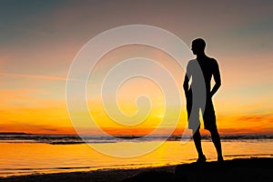 Young sporty man silhouette standing on the beach at sunset