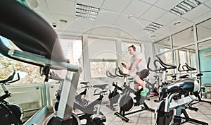 Young sporty man in white t-shirt and shorts is exercising bike at spinning class