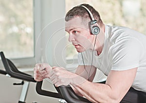 Young sporty man in white t-shirt and shorts is exercising bike at spinning class