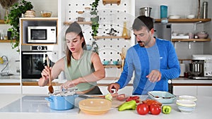 Young sporty man and woman couple cutting and together cooking fresh natural vegetables at kitchen and cooking for healthy lunch.