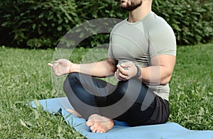 Young sporty man yogi sitting in lotus yoga pose in grass lawn park outdoors