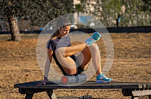 Young sporty runner in shorts leaning on a wooden table with her legs crossed up to the knee practicing a buttock self-massage