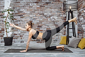 Young sporty slim woman doing yoga exercise at home stretching her arm to the front