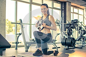 Young sporty woman in activewear doing exercises with weight-plate on fitness stepper in the gym