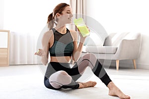 Young sporty woman with bottle of protein shake sitting