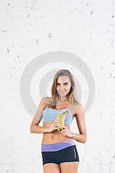 Young sporty woman in bright stylish sportswear holding bananas