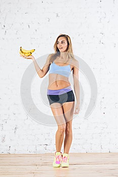 Young sporty woman in bright stylish sportswear holding bananas