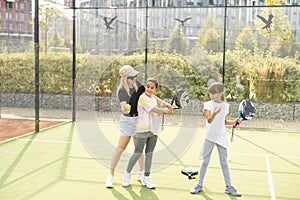 Young sporty woman with children playing padel game in court on sunny day