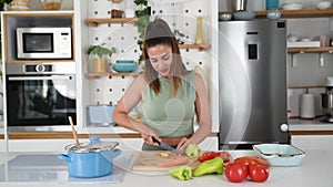 Young sporty woman cutting and cooking fresh natural vegetables at kitchen and cooking for healthy lunch. Self care yoga nutrition