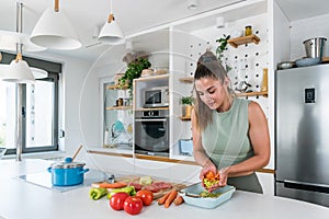 Young sporty woman cutting and cooking fresh natural vegetables at kitchen and cooking for healthy lunch. Self care yoga nutrition