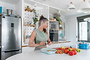 Young sporty woman cutting and cooking fresh natural vegetables at kitchen and cooking for healthy lunch. Self care yoga nutrition