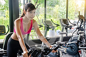 Young sporty woman cycling on bike machine in modern fitness gym,  Workout in Gym and fitness for health