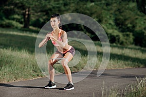 Young sporty woman doing squat exercises with rubber band outdoor.