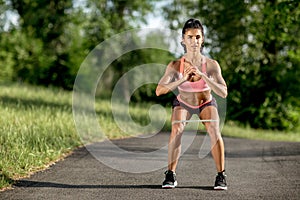 Young sporty woman doing squat exercises with rubber band outdoor.