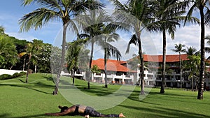 Young sporty woman doing yoga dog face down mountain pose outside in park with palm trees. Flexible girl practicing yoga