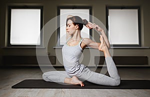 Young sporty woman doing yoga stretching exercise sitting in gym near bright windows