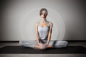 Young sporty woman doing yoga stretching exercise sitting in gym near bright windows