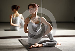 Young sporty woman doing yoga stretching exercise sitting in gym near bright windows