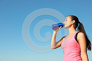 Young sporty woman drinking from water bottle outdoors on sunny day