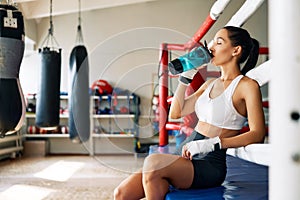 Young sporty woman drinking water after fight or workout exercising in boxing ring