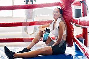 Young sporty woman drinking water after fight or workout exercising in boxing ring
