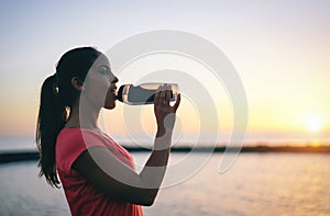 Young sporty woman drinking water while having a break - Health girl resting at sunset after running
