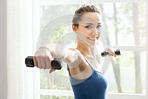 Young sporty woman exercising with dumbbells at home