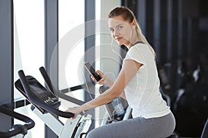 Young sporty woman in gym listen music from smartphone