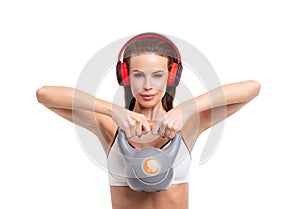 Young sporty woman in headphones holding kettlebell isolated