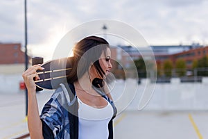 Young sporty woman holding longboard behind in sunset