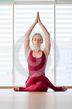 Young sporty woman practicing yoga on the background of a large window