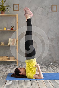 Young sporty woman practicing yoga at home, doing Salamba Sarvangasana exercise, supported shoulder stand pose.