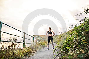 Young sporty woman runner in black activewear standing outside in nature, resting.