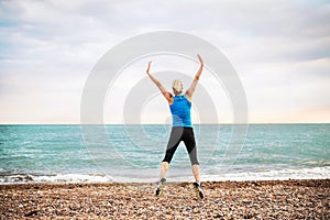 Young sporty woman runner in blue sportswear jumping on the beach outside.