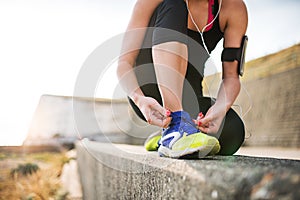 Young sporty woman runner with earphones tying shoelaces by the beach.