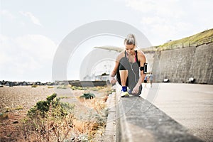 Young sporty woman runner with earphones tying shoelaces by the beach.