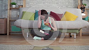 Young sporty woman sitting on the floor looking at the bathroom scales eating a Burger