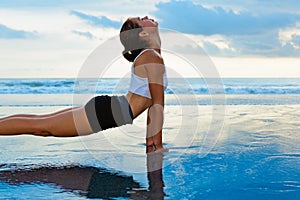 Young sporty woman stretching on sunset beach