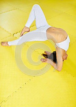 Young sporty woman in white sportswear practicing yoga on yellow mat in a gym. Healthy lifestyle, morning exercises