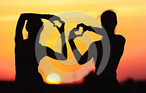 Young sporty women holding hands in heart shape at sunset