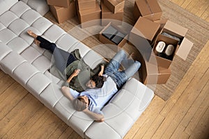 Young spouses modern apartment owners cuddle on couch among boxes