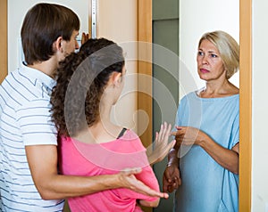 Young spouses receiving irritated senior neighbor at doorway photo